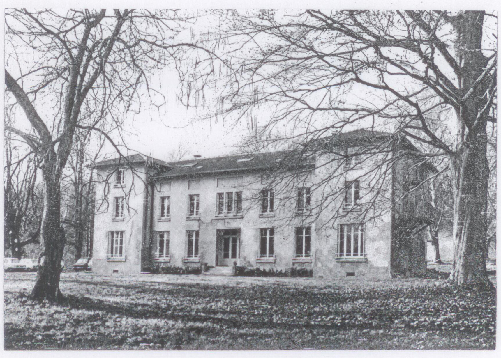 Photographie d'un grand bâtiment à deux étages au milieu d'un parc aux grands arbres dénudés