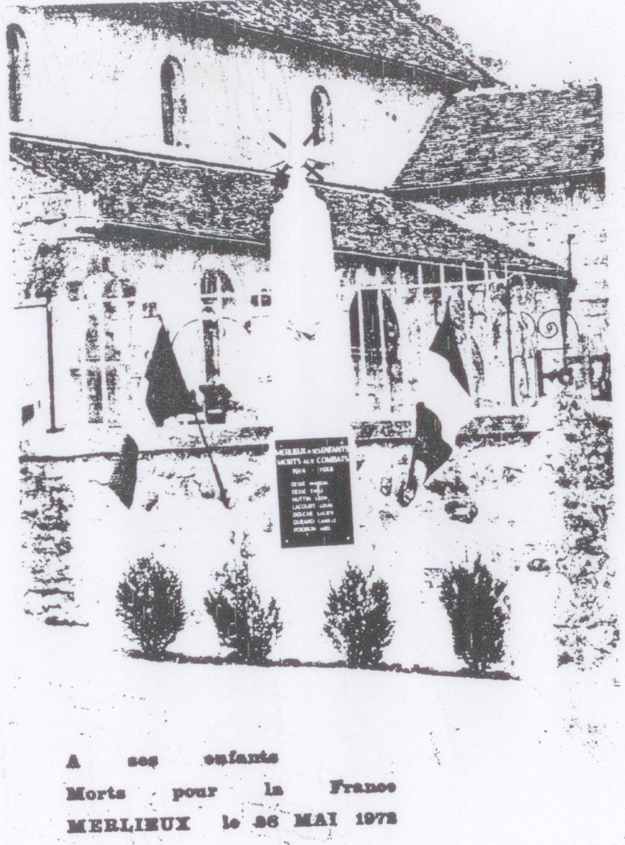 Photographie du monument aux morts devant l'église, avec une plaque portant les noms des morts de 1914-1918, des drapeaux et quatre arbustes